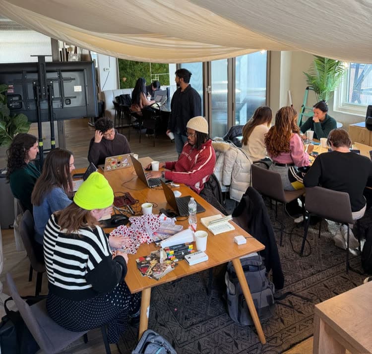 Members working on laptops at long tables under a draped canopy